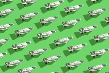Patterns of dollars folded into origami planes on a green background with hard shadows..