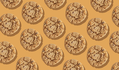 Patterns of round light cookies with chocolate chips and hard shadows on an orange background.