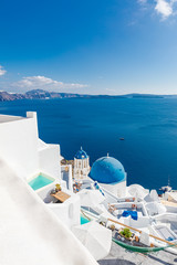 Beautiful Oia town on Santorini island, Greece. Traditional white architecture and greek orthodox churches with blue domes over the Caldera, Aegean sea. Scenic luxury travel background.