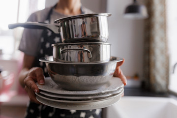 girl in an apron holds dishes, pots and kitchen utensils