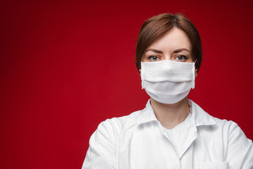 Portrait of medic in white medical coat and protective mask posing isolated on blue background. Protection and safety concept