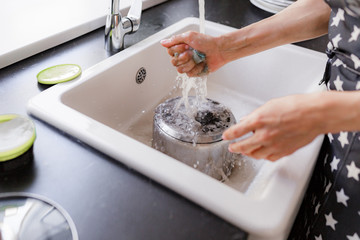 girl in an apron washes dishes in the kitchen, daylight.