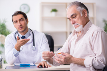 Young male doctor and old patient in antismoking concept