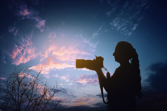 Silhouette of a woman photographer with dslr camera during taking photos at sunset