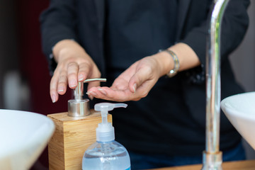 Business woman in dark black suit is puhsing washing soap on her hand beside the sink.