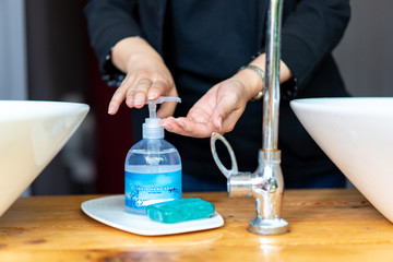 Business woman in dark black suit is puhsing washing soap on her hand beside the sink.