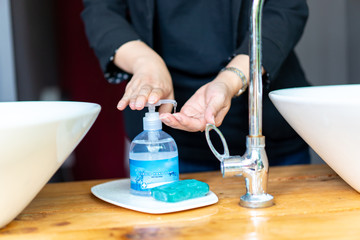 Business woman in dark black suit is puhsing washing soap on her hand beside the sink.