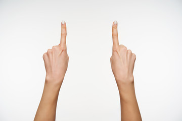 Indoor photo of pretty woman's hands keeping forefingers raised while pointing upwards, isolated over white background while expressing body language