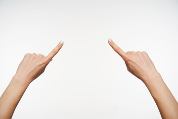 Horizontal photo of lady's hands showing in one point with raised index fingers while posing over white background. Women showing hand with sign language