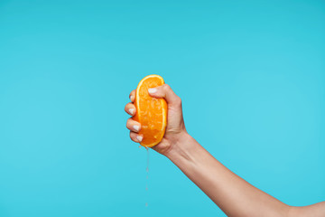 Indoor photo of young attractive hand holding orange and clenching a fists while queezing juice,...