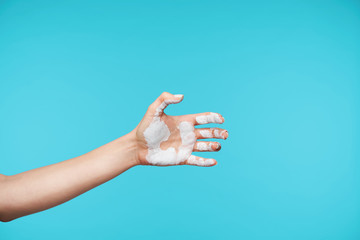 Side view of young woman's hand being raised while going to shake hand, but realising that it is dirty and squeezing arm, isolated over blue background
