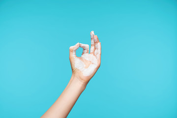 Photo of painted in white color hand being raised while showing mudra gesture, posing over blue...