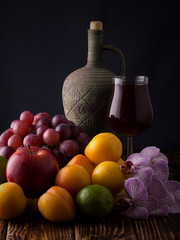 red wine and clay vessel with fruits and grapes on a wooden table.