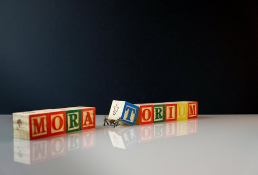 Conceptual of moratorium granted by banks during financial crisis and recession. Miniature workers separating wooden alphabet cubes TORIUM over dark background. Focus on selective cubes .