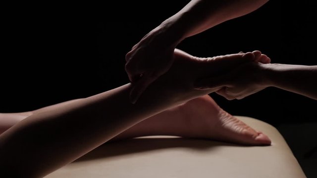 Foot massage closeup on a black background. Female legs. Slow motion.