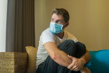 covid-19 virus lockdown - sad and worried man in medical mask thinking and feeling scared in quarantine following stay at home instructions to contain virus pandemic