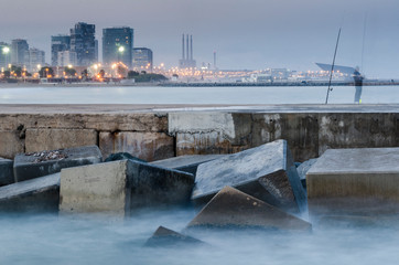 Paisaje urbano desde la playa de Barcelona al anochecer con la silueta de un pescador con la...
