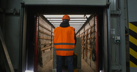 warehouse worker driver in uniform loading cardboard boxes by forklift stacker loader