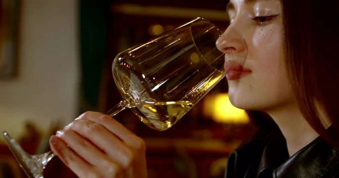 young pretty woman is sipping white wine from glass in restaurant