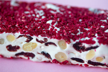 Torrone or nougat bar with nuts and red dried berries. Traditional italian dessert close up on pink background. Sweet tasty and healthy food