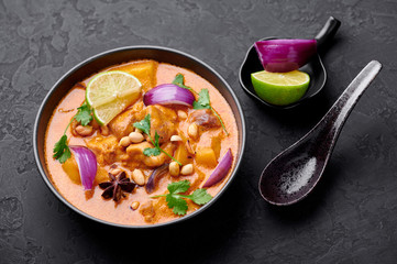 A Chicken Massaman Curry in black bowl at dark slate background. Massaman Curry is Thai Cuisine dish with chicken meat, potato, onion and many spices. Thai Food.