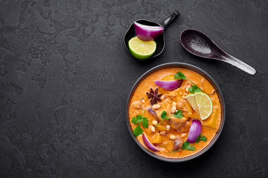A Chicken Massaman Curry in black bowl at dark slate background. Massaman Curry is Thai Cuisine dish with chicken meat, potato, onion and many spices. Thai Food. Copy space. Top view