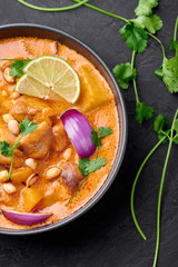 A Chicken Massaman Curry in black bowl at dark slate background. Massaman Curry is Thai Cuisine dish with chicken meat, potato, onion and many spices. Thai Food. Close up