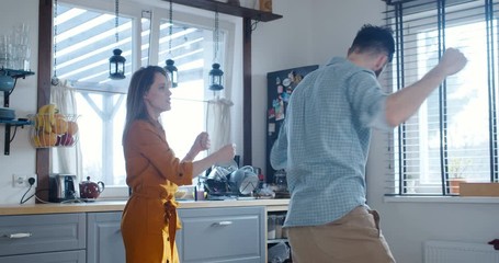 Happy young fun energetic Caucasian man and woman dance like crazy at breakfast in modern light kitchen slow motion. - Powered by Adobe