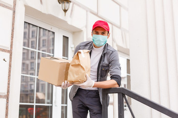 Courier in protective mask and medical gloves delivers takeaway food. Delivery service under quarantine, disease outbreak, coronavirus covid-19 pandemic conditions.