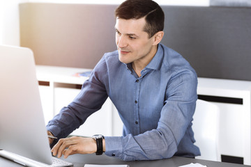 Businessman working with computer in modern sunny office. Headshot of male entrepreneur or company...