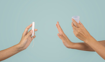 Zero waste alternative consept. Tampon vs menstrual cup. Woman hands on pastel mint background. hygiene period product.