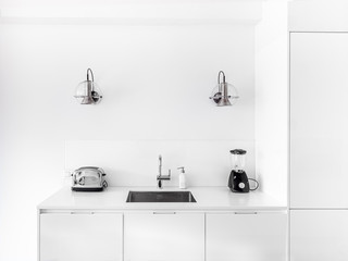 New stylish bright kitchen with white cabinets. Spacious modern interior with metal sink, retro lamps and black equipement.