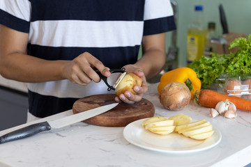 man peeling and cutting a potato on a white kitchen table with vegetables in the background