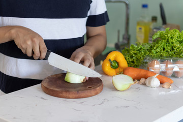 man cutting a onion with a knife on a white kitchen table with vegetables in the background