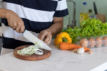man cutting a onion with a knife on a white kitchen table with vegetables in the background