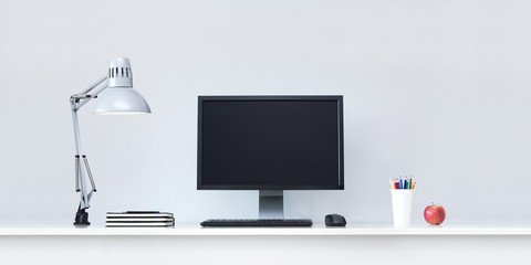 Clean white office desk in with computer and lamp.