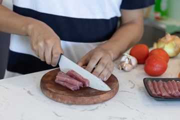 man cutting a piece of beef white a knife on a white kitchen table with vegetables in the background