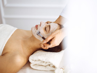 Obraz na płótnie Canvas Beautiful brunette woman enjoying applying cosmetic mask with closed eyes. Relaxing treatment in medicine and spa center concepts