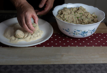 Male hands coating in breadcrumbs tuna meatballs.