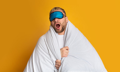 Guy in mask for sleep yawns in blanket