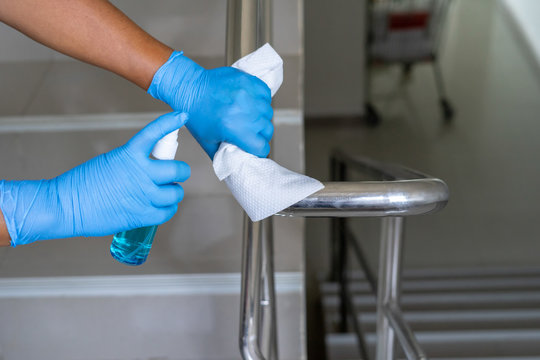 Close up of female hand using wet wipe and hand sanitizer spray to clean stainless steel staircase railing.Antiseptic,disinfection ,cleanliness and healthcare,anti virus concept.Anti bacterial and Cor