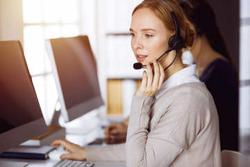 Businesswoman talking by headset in sunny office. Call center and diverse people group in business