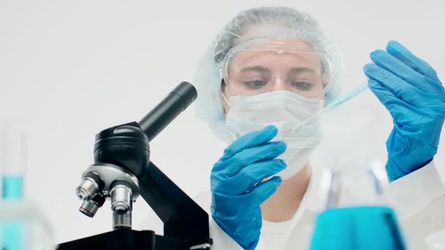 Cute laboratory assistant in protective equipment drips samples