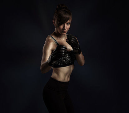 Sport fight concept with copy space. Portrait of kickboxing woman in black boxing gloves and grey sports bra and panties posing on black