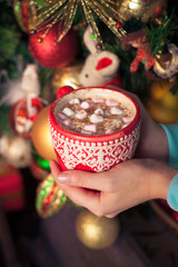 a cup of aromatic cocoa with marshmellow in the hands just before christmas eve