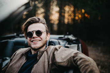 young male driver in sunglasses in a convertible in the summer at sunset. travel concept.