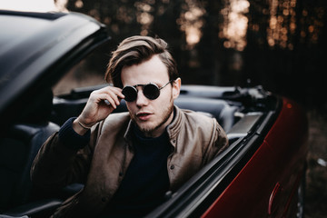 young male driver in sunglasses in a convertible in the summer at sunset. travel concept.