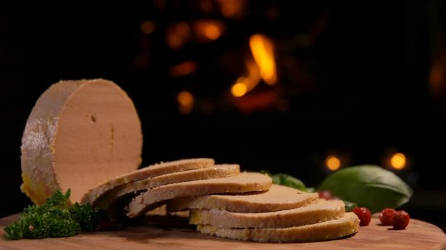 Panorama of sliced foie gras on a wooden board with parsley on the background of a burning fireplace