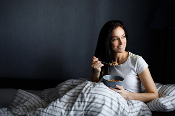 Fototapeta premium Breakfast woman with yoghurt cereal lying in bed eating a healthy snack with fruit and carefree smile