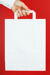 Paper bag at arm's length, white craft bag for takeaway isolated on red background. Packaging template layout with space for copying, advertising.